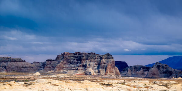 Arizona landscape scene of the sun shining on sand dunes and rocky buttes with dark storm clouds overhead on the shore of Lake Powell