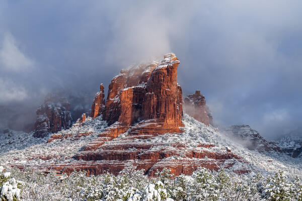 Sedona lanscape scene of a red rock mountain covered in snow and emerging through the clouds