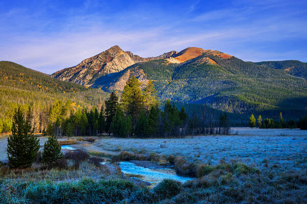 Mountains in the background behind a meadow and a stream in Rocky Mountain National Park