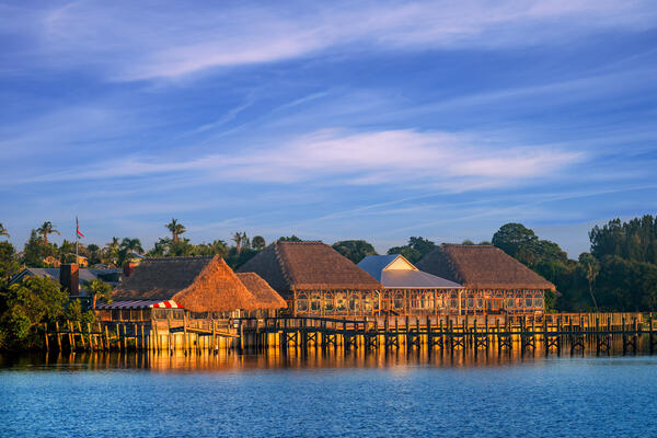 Thatch covered tiki structures on the water's edge with sunrise light
