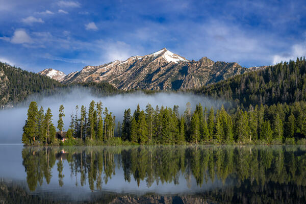Idaho landscazpe scene of a view of early morning fog over the water at Pettit Lake near Stanley Idaho with snow-capped Sawtooth Mountains