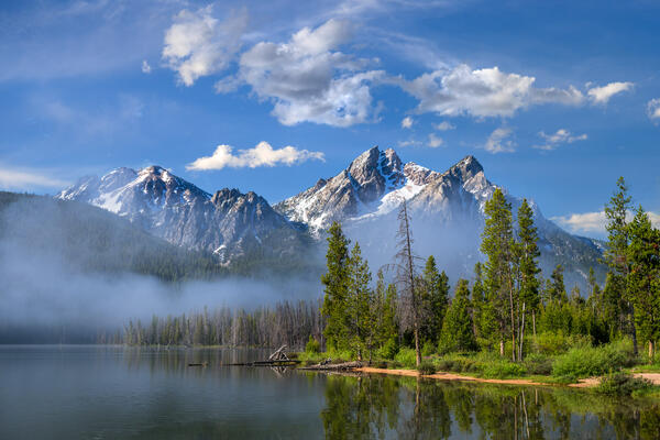 Idaho landscazpe scene of a view of Stanley Lake with fog over the water and McGown Mountain towering above it all.