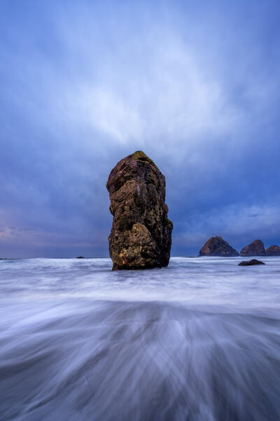 Oregon Coast landscape scene of a long exposure used to highlight the ocean waves receding back out to a large sea stack at Pistol River