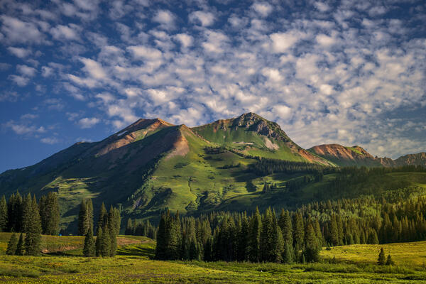 Colorado landscape view of a mountain with an incredible sky of many clouds and lush greenery of the summer.