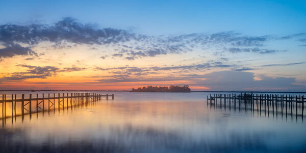 Florida landscape scene of sunrise over two docks and an island reflecting in the water of the Indian River